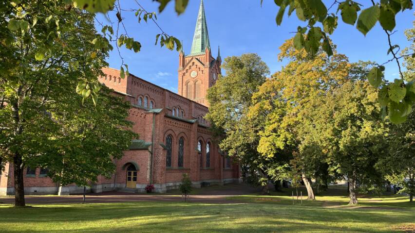 Uudenkaupungin Uusi kirkko, punainen tiilikirkko. Vihreä nurmialue puineen kirkon edessä.