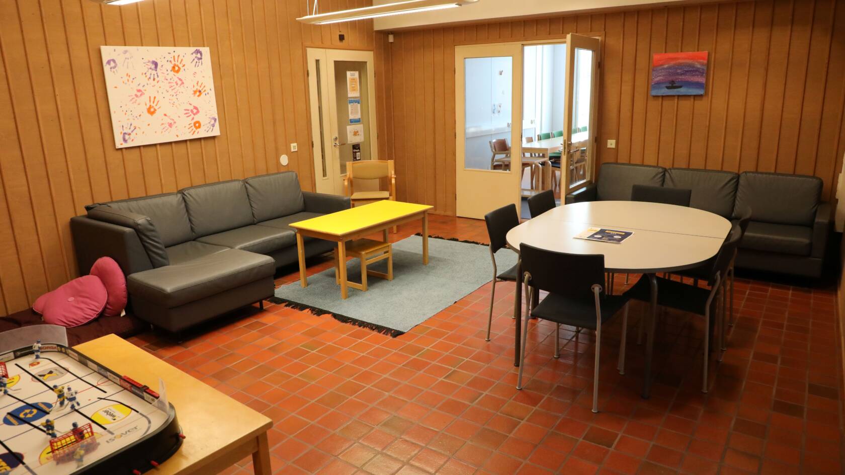 Huone, jossa on sohvia, pöytäryhmä niin aikuisille kuin lapsille. Edessä pöydällä jääkiekkopöytäpeli.