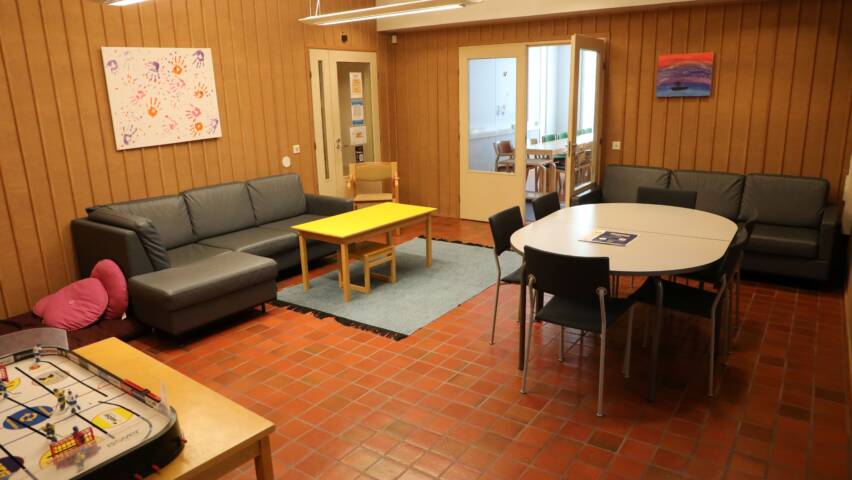 Huone, jossa on sohvia, pöytäryhmä niin aikuisille kuin lapsille. Edessä pöydällä jääkiekkopöytäpeli.