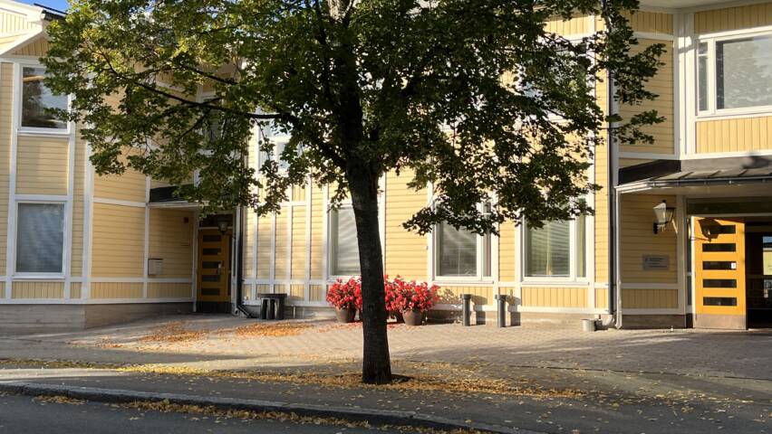 Seurakuntakeskus pääovien julkisivu, väriltään keltainen. Etuosaa peittää puu.