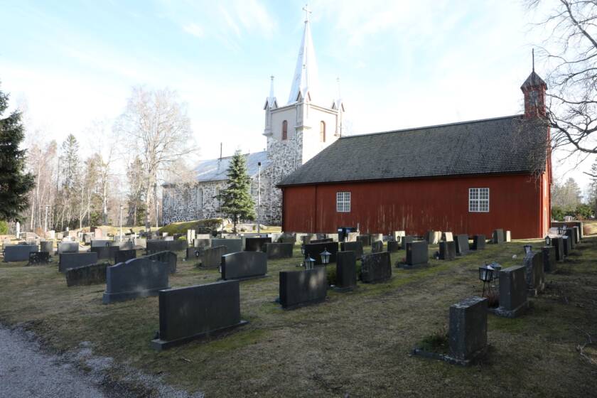 Pyhämaan punainen uhrikirkko, taustalla kivikirkko kirkon torneineen, kuva otettu hautausmaalta.