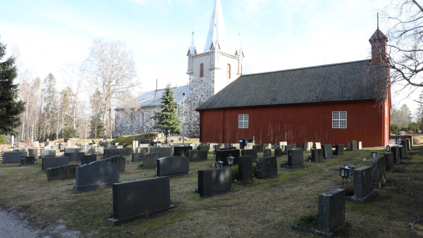 Pyhämaan punainen uhrikirkko, taustalla kivikirkko kirkon torneineen, kuva otettu hautausmaalta.