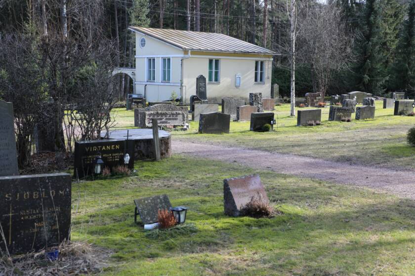 Hautakivet riveissä hautausmaalla, taustalla näkyy keltainen ruumishuone.