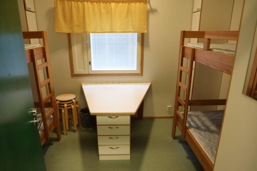 Huone, jossa on molemmilla reunoilla kerrossängyt, keskellä kiinteä pöytä.