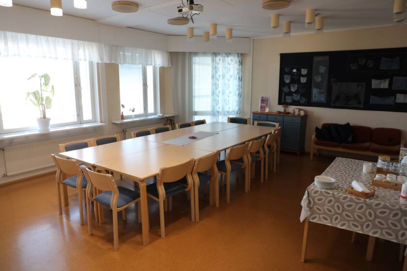 Kokouspöytäryhmä keskellä huonetta, sivussa tarjoilupöytä.
