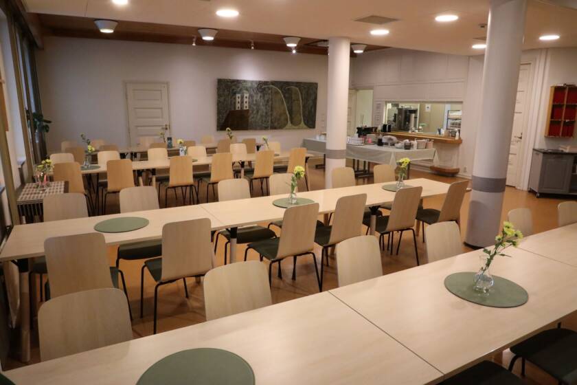 Seurakuntakeskuksen kahvion pöytäryhmät, taustalla tarjoilukeittiö.