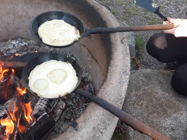 Kuvassa nuotio ja kaksi lettupannua. Pannuissa paistumassa lettuja
