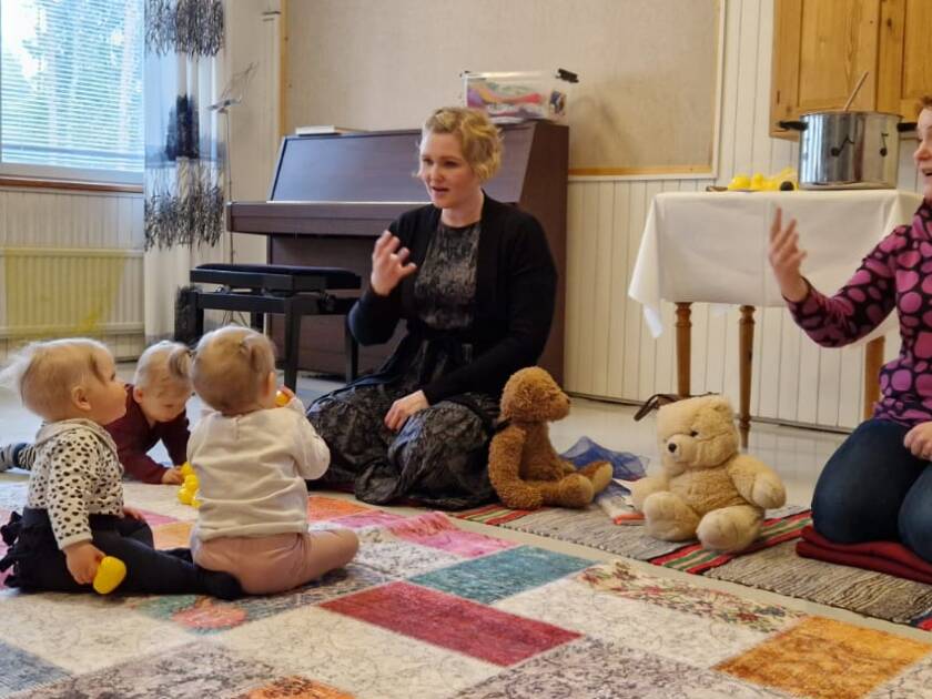 kaksi aikuista ja muutamia lapsia muskarissa istumassa lattialla.