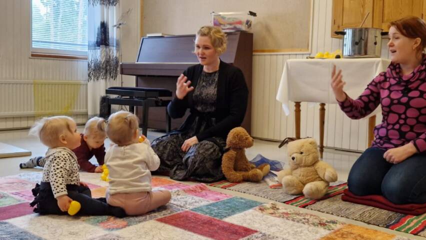kaksi aikuista ja muutamia lapsia muskarissa istumassa lattialla.