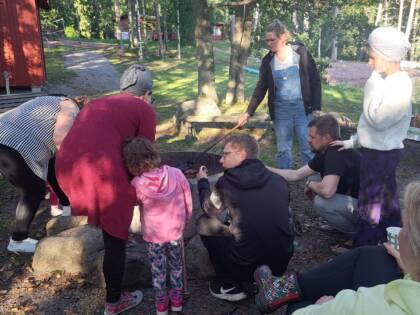 Kuvassa aikuisia ja lapsia nuotiolla paistamassa jotakin.