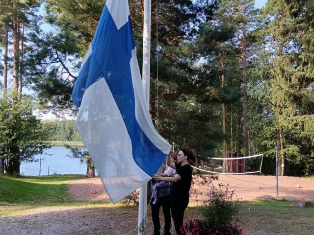 Kuvassa kaksi ihmistä nostamassa suomenlippua.