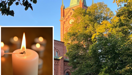 Kesäinen kuva Uudenkaupungin Uuden kirkosta, kuva kohdistettu tapuliin, ympäröivät puut lehdessä, aurinko paistaa.