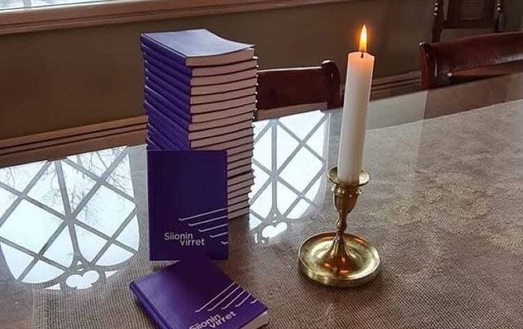 Siioninvirsiseurojen mainoskuva, kuva Uudenkikon sakastin pöydästä jolla palaa kynttilä, kynttilän edessä pino violetteja siioninvirsikirjoja.